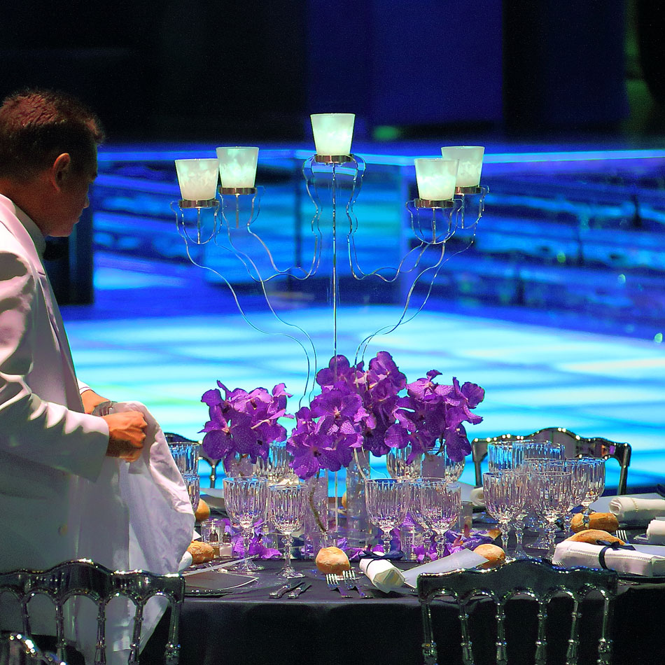 Candlelit table with orchids in front of a lit stage